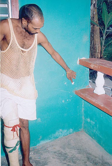 The dead woman's son, Mohammed Sharief Alli points to the bullet holes in the wall where he was seated with the neighbour when the incident occurred.